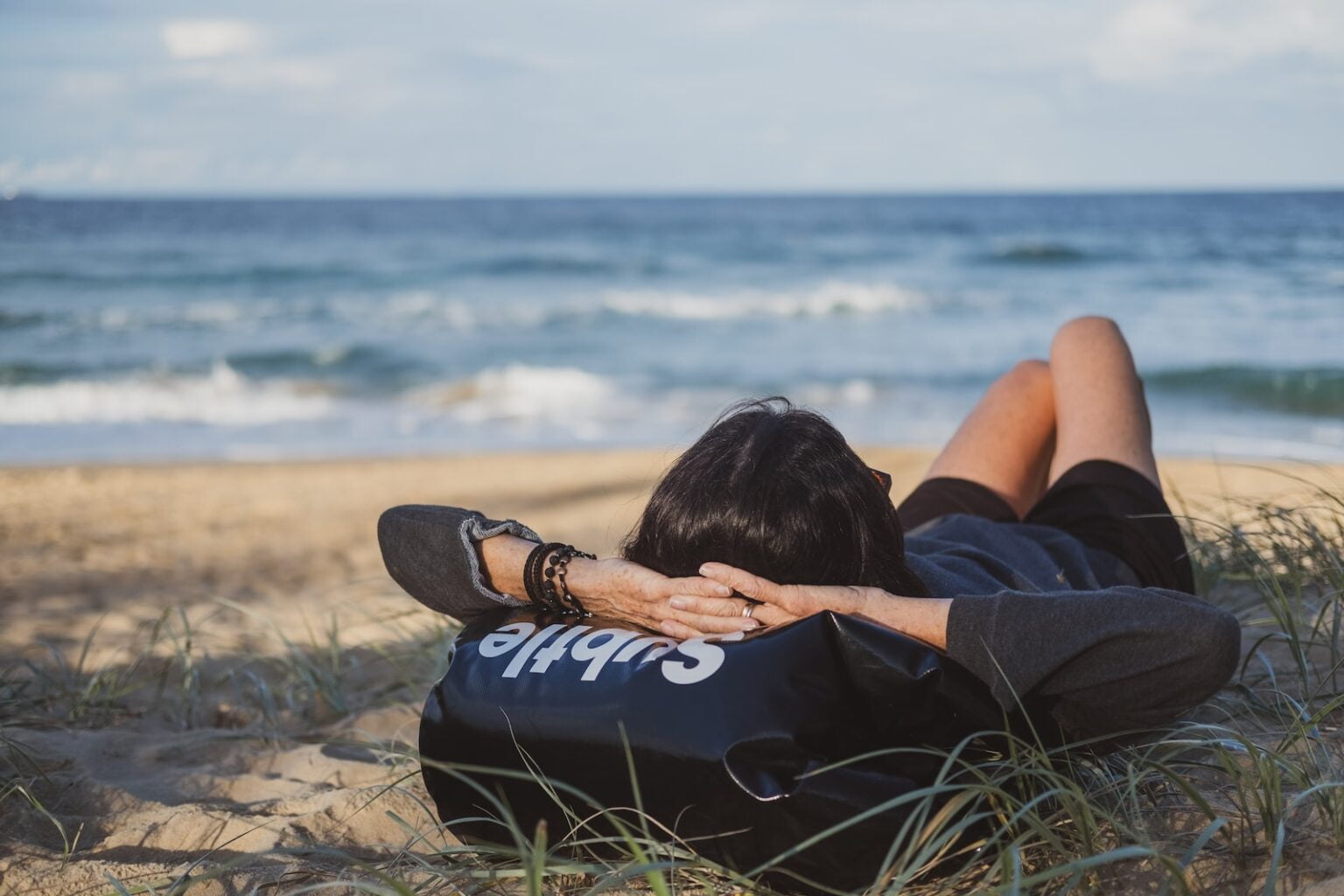 woman lying on grass front of sea at daytime - sleeping on beach - backpacker accommodation