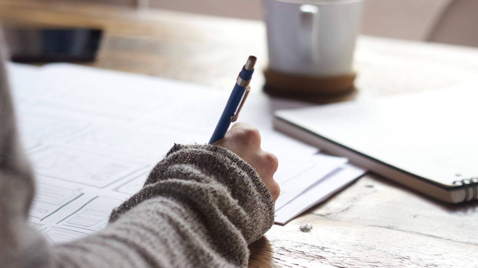 Getting your working holiday visa to australia 2 Person writing on brown wooden table near white ceramic mug - planning working holiday visa - backpacker visas